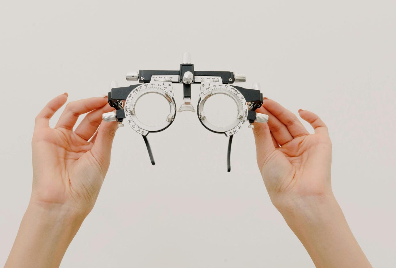 Crop unrecognizable female demonstrating modern trial frame with optical lenses against white background in optometrist studio